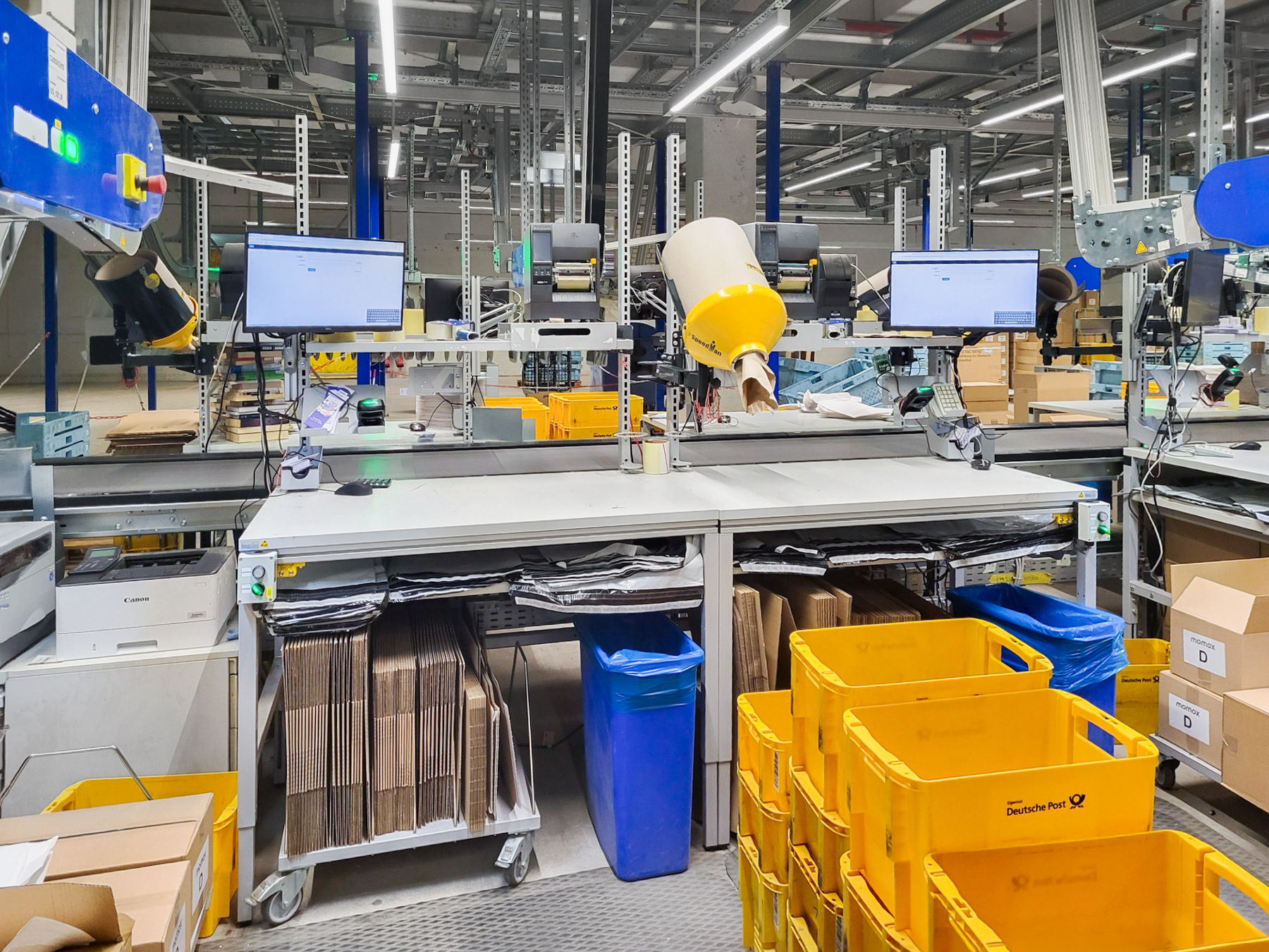 ERGO-line packing table for use in logistics, featuring monitors, a scanner, a storage shelf, a mobile folding-box magazine and shelving